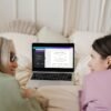 Mother and daughter happily editing a marriage licence template on a laptop in a cozy bedroom.